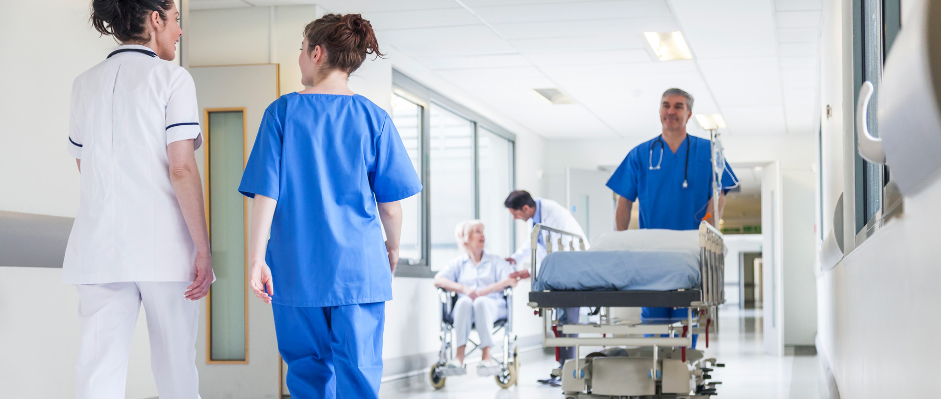 infermiere con camice blu spinge lettino vuoto in corsia di ospedale