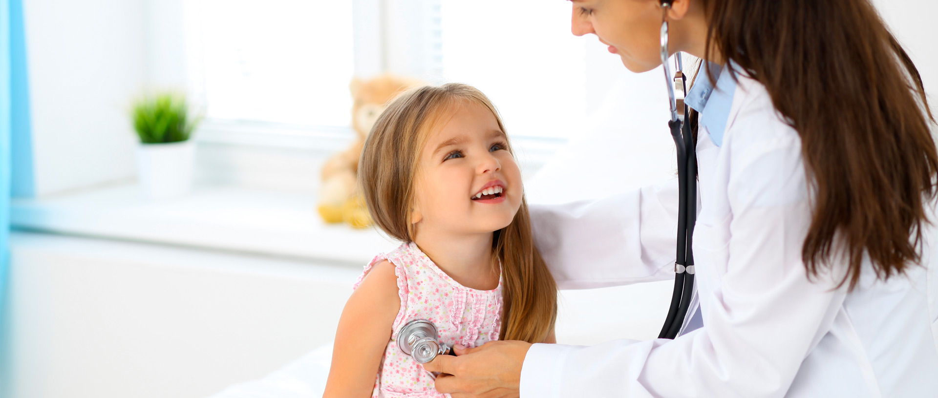giovane pediatra donna ausculta cuore di bimba bionda sorridente